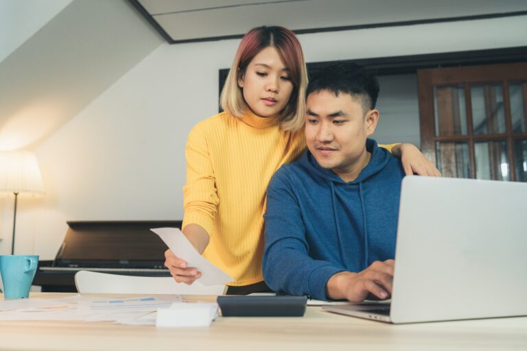 Young asian couple reviewing their bank accounts using laptop computer and calculator at home.